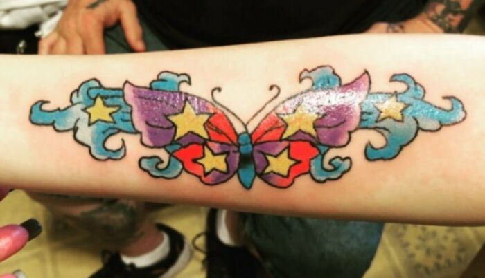 Colorful butterfly tattoo with stars, possibly a funny worst tattoo fail, on forearm.