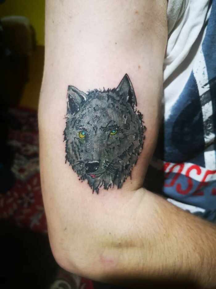 Wolf tattoo on arm with uneven coloring, capturing funny tattoo fails humor.