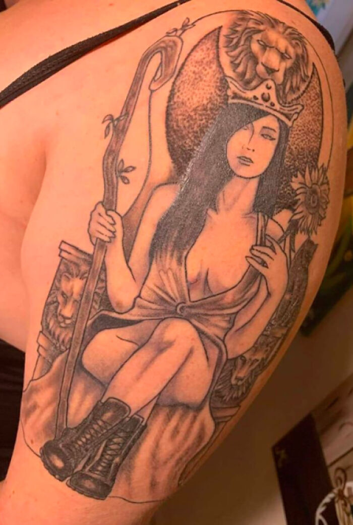 A tattoo fail with a seated woman wearing a crown and boots, surrounded by a lion and sunflowers.
