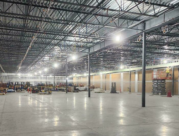 Workers blatantly ignoring safety protocol inside a large warehouse under construction with exposed beams and equipment.
