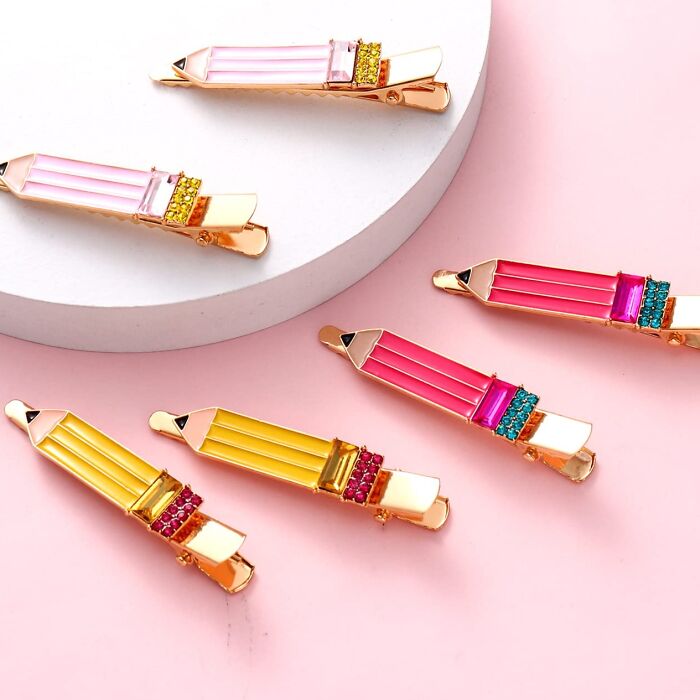Colorful pencil-shaped hair clips on a pink background, ideal gifts for teachers.