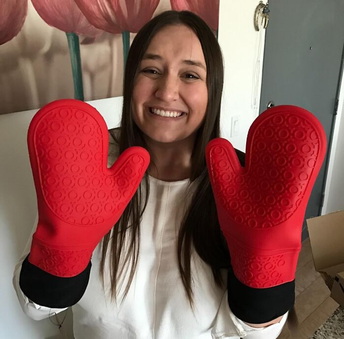 Woman smiling while wearing red clever oven mitt inventions indoors.
