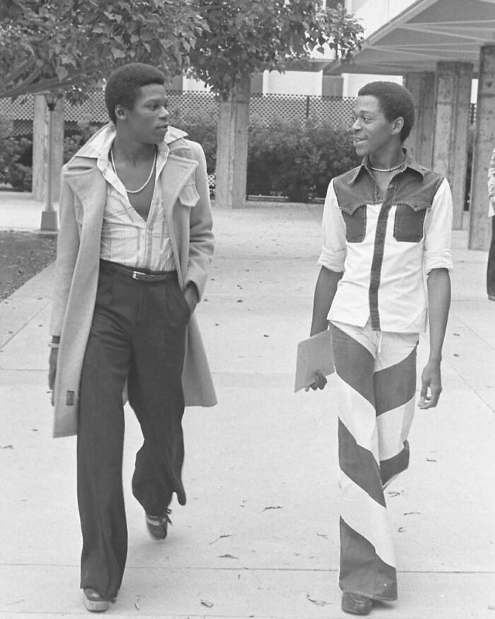 Two students walking, showcasing '70s high school fashion with bell-bottoms and layered shirts. Two students walking, showcasing '70s high school fashion with bell-bottoms and layered shirts.