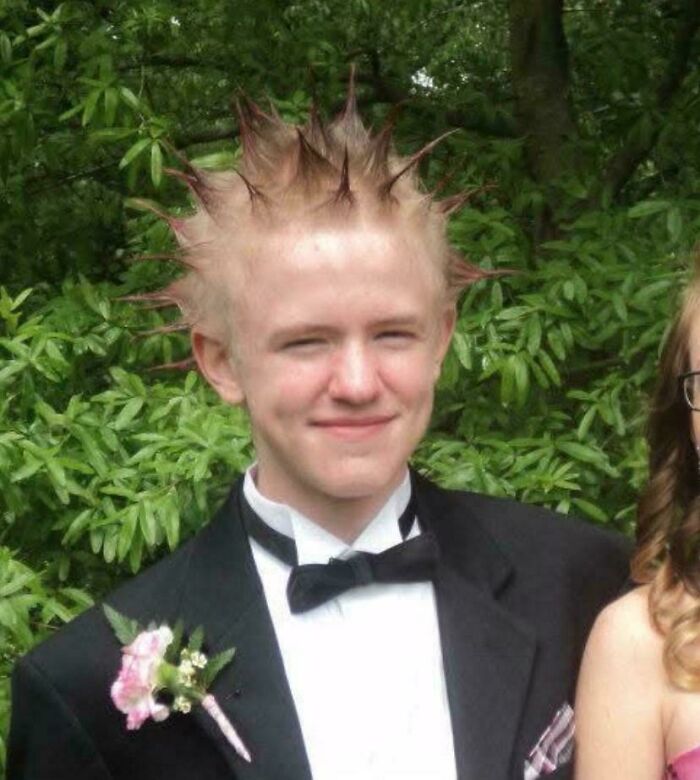 Teen with spiked hair and a tuxedo, representing embarrassing blunder years, standing outdoors with greenery background.