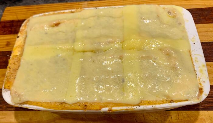 Casserole dish with cheese-covered topping, resembling an unevenly baked lasagna, on a wooden surface.
