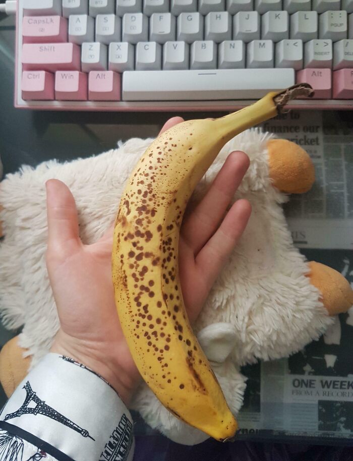 Hand holding a spotted banana over a desk with a keyboard, illustrating a quirky family moment.