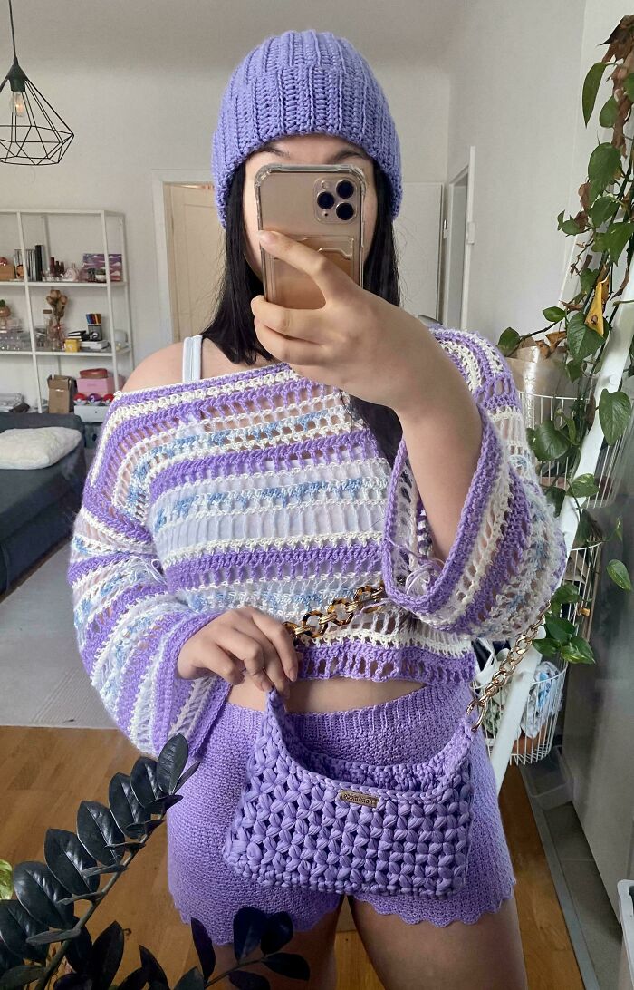 Young woman showcasing her proud crochet project wearing a lavender crochet top, shorts, hat, and matching bag.