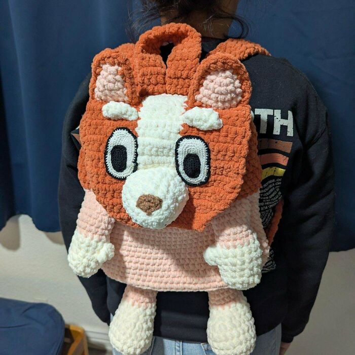 Person wearing a handmade crochet backpack shaped like an animal, showcasing a proud crochet project by enthusiasts.