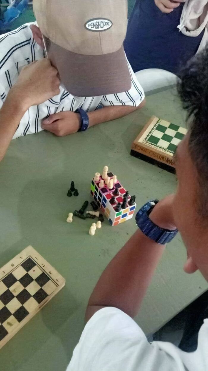Two people playing chess with pieces on a Rubik’s Cube, combining science and humor.