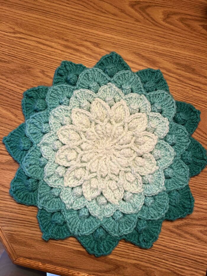 Crochet project featuring a layered flower design in shades of green on a wooden surface.