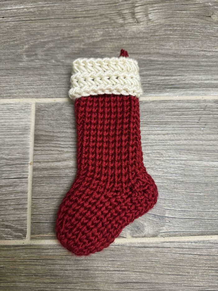 Small red and white crochet Christmas stocking placed on a wooden floor, showcasing a proud handmade project.