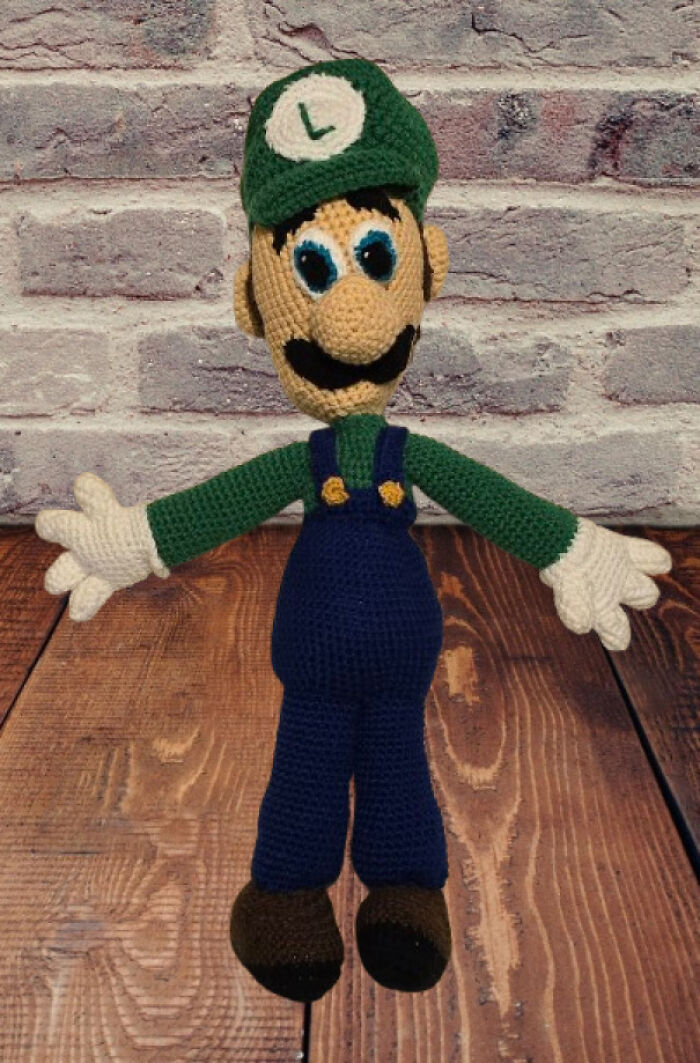 Crochet enthusiast’s detailed handmade Luigi doll with green hat and blue overalls displayed on wooden surface.
