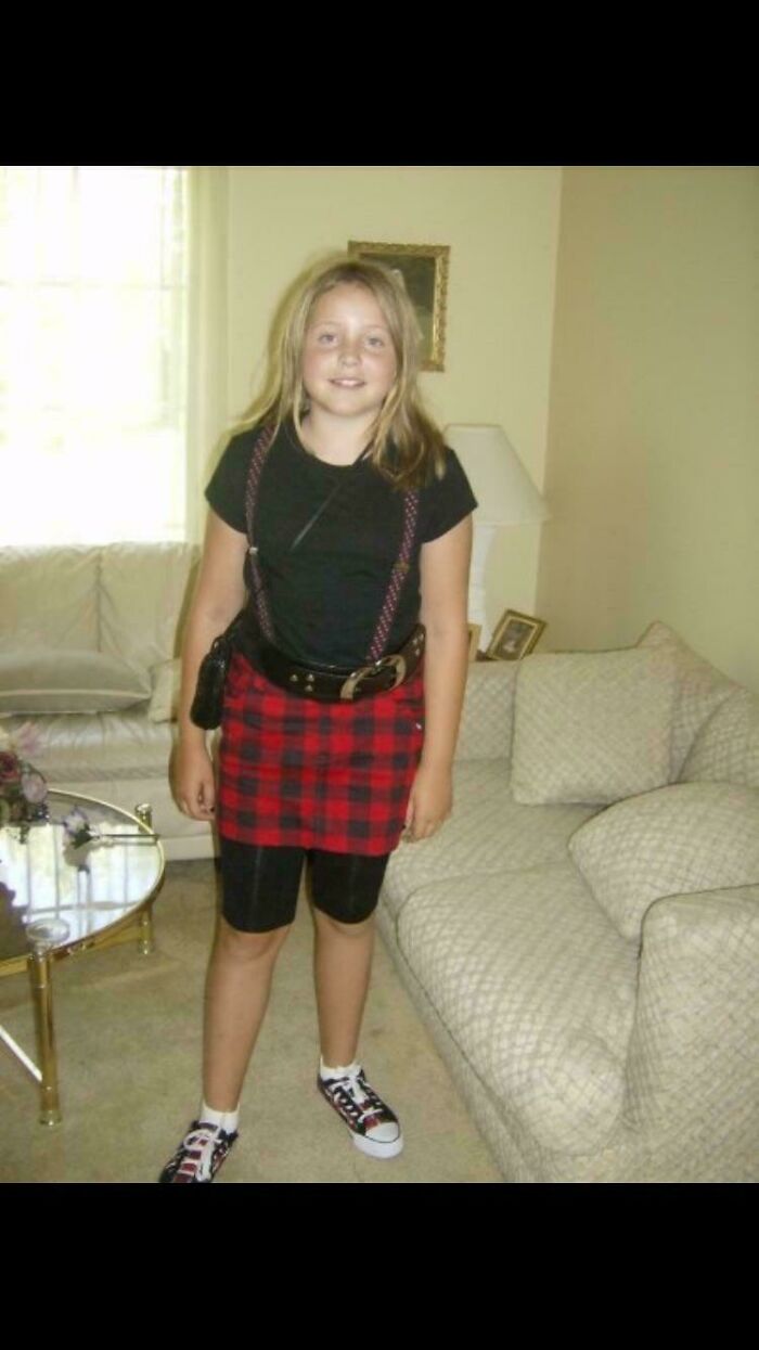 Girl in childhood photo wearing a plaid skirt and black shirt, embodying blunder years fashion.