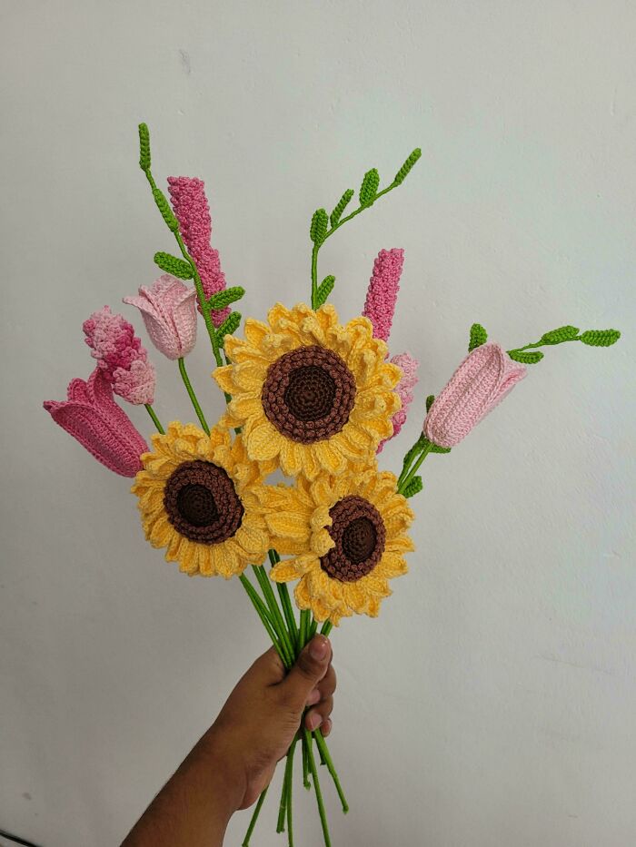 Hand holding a bouquet of crocheted sunflowers and pink flowers showcasing crochet enthusiasts proud project.