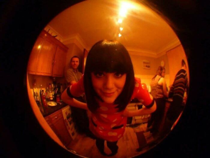 Fisheye lens photo capturing a woman's quirky pose in a retro room, epitomizing "Blunder Years."