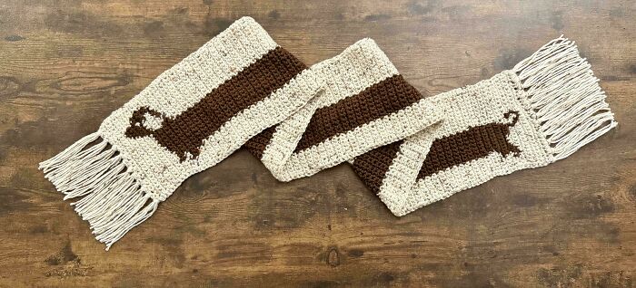 Handmade crochet scarf with otter designs and fringed ends laid out on a wooden surface by crochet enthusiasts.
