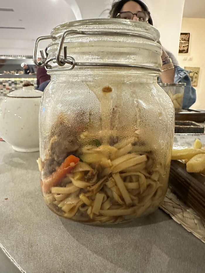 Noodles and vegetables served inside a large glass jar, showcasing one of the most ridiculous food serving ideas in restaurants.