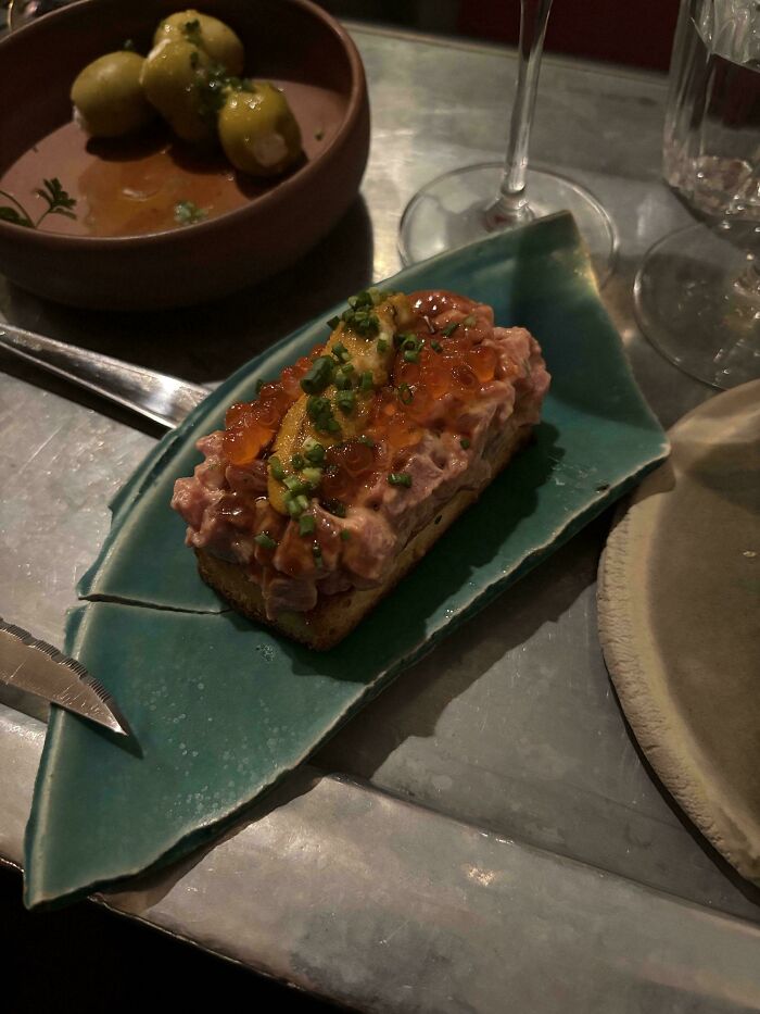 Unusual food plating on a broken ceramic leaf-shaped dish showing a seafood appetizer in a restaurant setting.