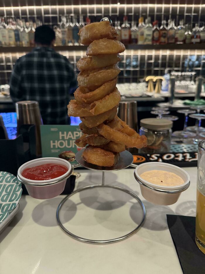 Onion rings stacked on a metal stand with ketchup and dipping sauce, an unusual food presentation in restaurants.