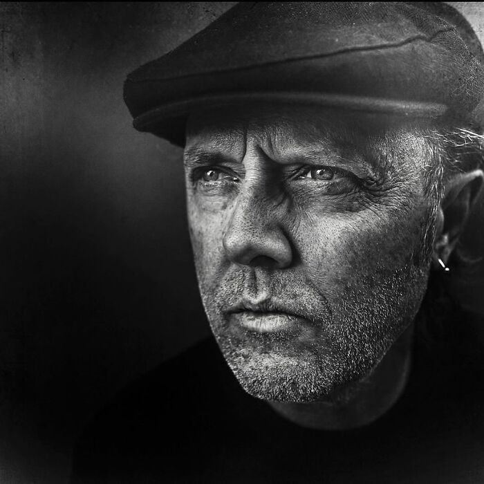 Black and white portrait by Lee Jeffries of a man wearing a flat cap, looking pensive with a rugged face.