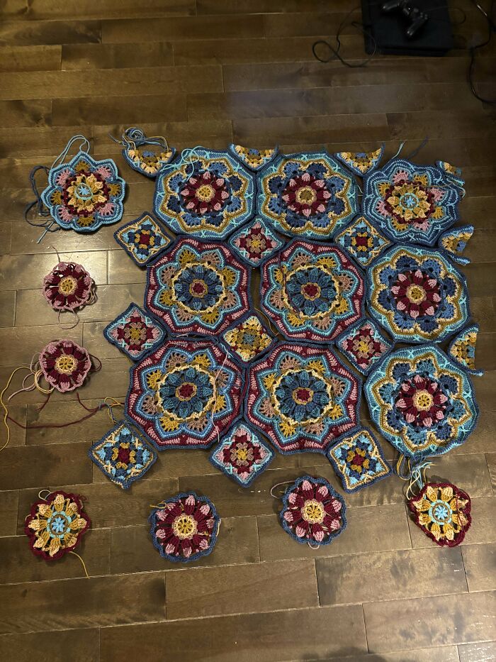 Colorful crochet project with floral and geometric patterns laid out on wooden floor by crochet enthusiasts.