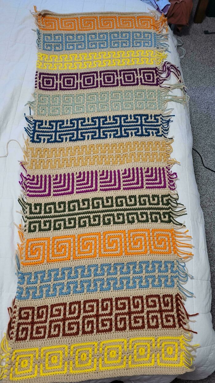 Crochet blanket with colorful geometric patterns and fringed edges, showcasing a proud crochet enthusiast’s project.