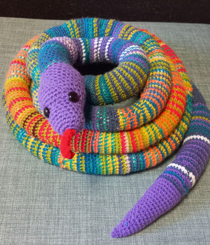 Crochet enthusiast’s colorful striped snake project coiled on a gray surface, showcasing detailed handmade stitches.