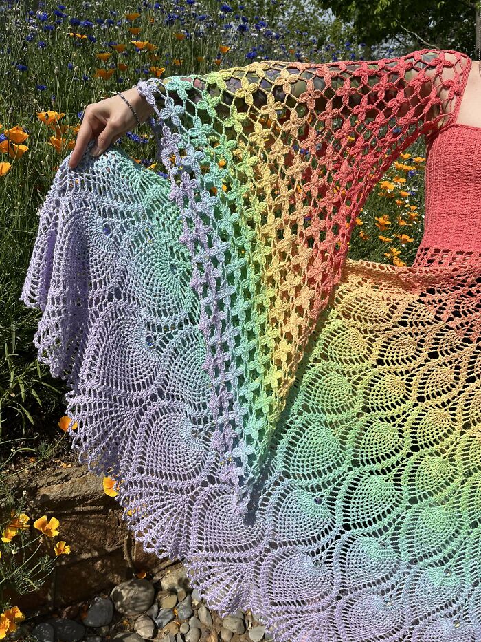 Colorful crochet shawl with intricate patterns displayed outdoors among flowers by crochet enthusiasts proud of their projects