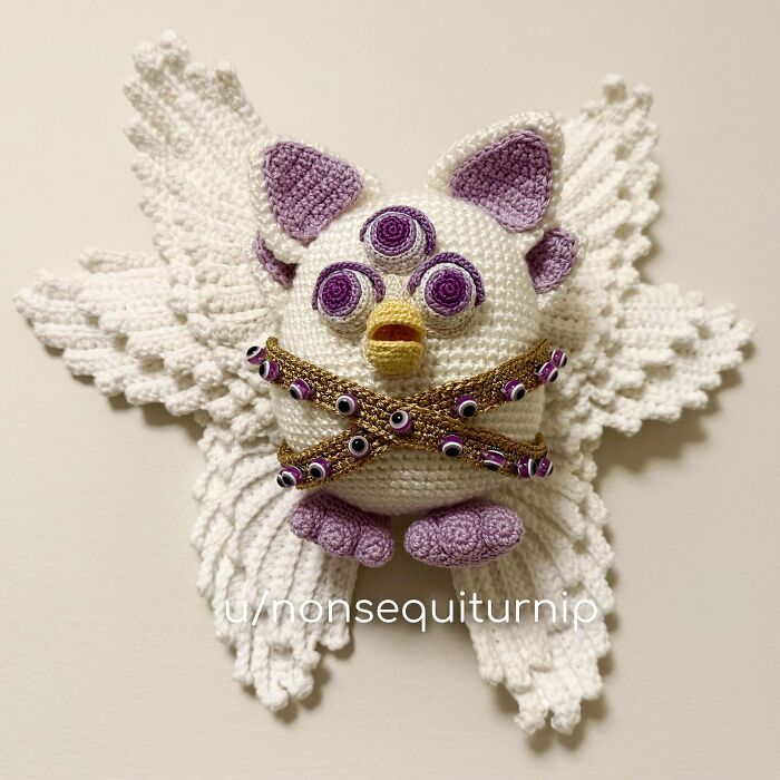 Crochet enthusiast's detailed amigurumi project featuring a three-eyed creature with wings and intricate beadwork.