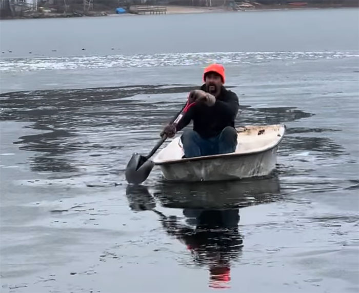 Man in a boat on icy lake rescuing a cat stuck on an ice chunk. Man in a boat on icy lake rescuing a cat stuck on an ice chunk.
