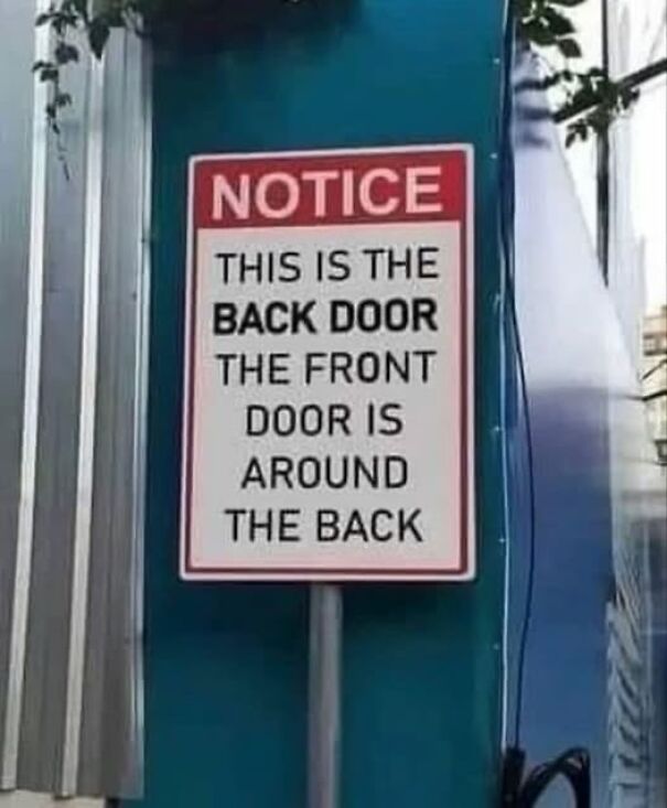 Weird sign: "This is the back door, the front door is around the back" on a post.