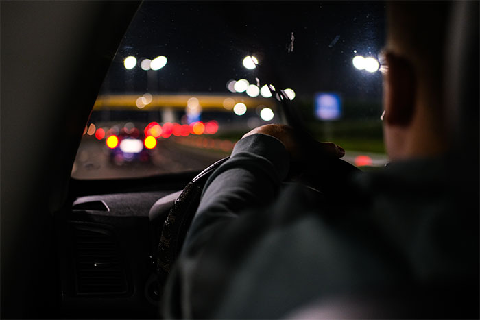 A person driving a car at night during the holiday season with city lights blurred in the background. A person driving a car at night during the holiday season with city lights blurred in the background.