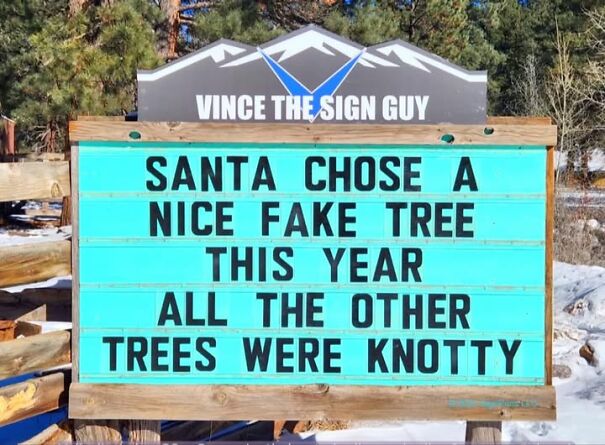 Weird and absurd sign about Santa choosing a fake tree because others were knotty, displayed outdoors by Vince The Sign Guy.