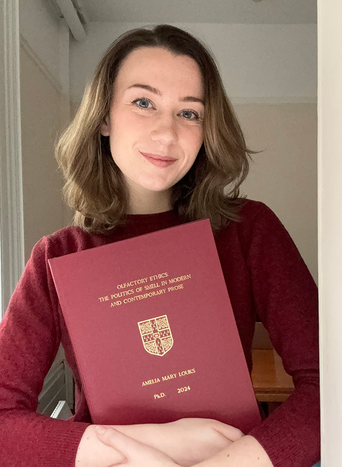 Dr. Ally Louks holding her thesis titled "Olfactory Ethics: The Politics of Smell" in a maroon cover. Dr. Ally Louks holding her thesis titled "Olfactory Ethics: The Politics of Smell" in a maroon cover.