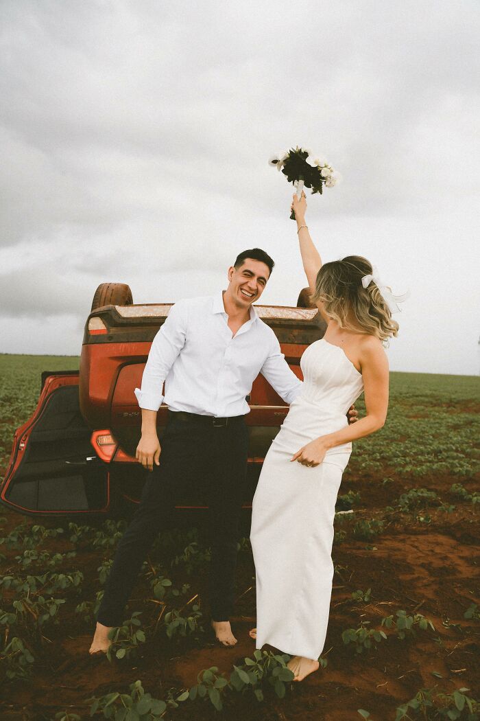 Couple poses joyfully in front of overturned car after accident on way to photo shoot, capturing a unique moment. Couple poses joyfully in front of overturned car after accident on way to photo shoot, capturing a unique moment.