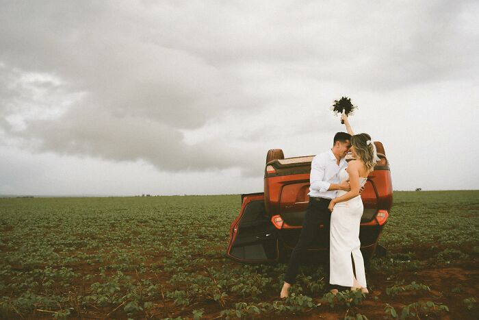 Couple poses for a photo in front of their overturned car in a field, showcasing resilience at accident scene. Couple poses for a photo in front of their overturned car in a field, showcasing resilience at accident scene.
