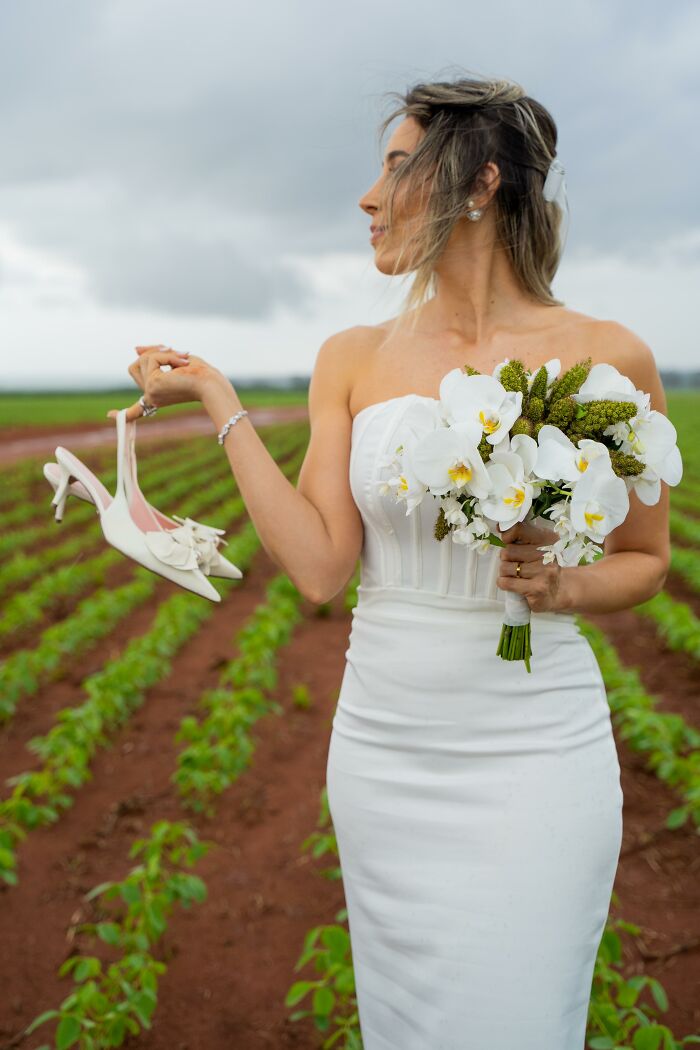 Bride holding shoes and bouquet in a field after a car accident on the way to a photoshoot. Bride holding shoes and bouquet in a field after a car accident on the way to a photoshoot.