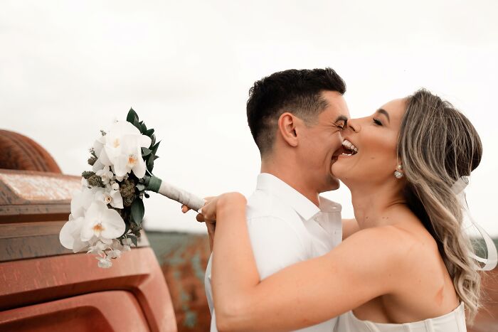 Couple smiling and embracing by overturned car, holding a bouquet, capturing moments after accident on the way to photo shoot. Couple smiling and embracing by overturned car, holding a bouquet, capturing moments after accident on the way to photo shoot.