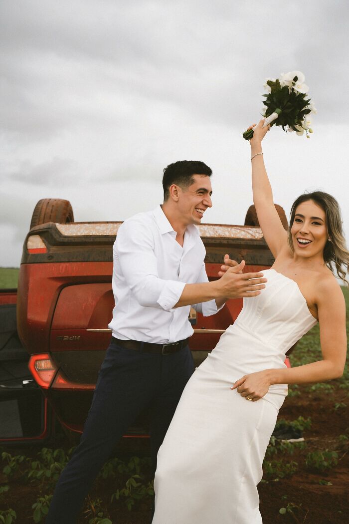 Couple poses joyfully in wedding attire beside overturned car after accident on the way to their photo shoot. Couple poses joyfully in wedding attire beside overturned car after accident on the way to their photo shoot.
