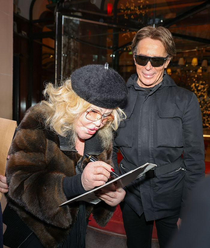 Jocelyn Wildenstein in Paris, wearing a fur coat and beret, with fiancé beside her, holding a clipboard. Jocelyn Wildenstein in Paris, wearing a fur coat and beret, with fiancé beside her, holding a clipboard.