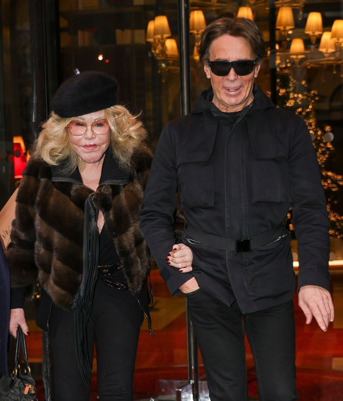 Jocelyn Wildenstein with smooth skin in Paris, wearing dark glasses and a fur coat, walking with a man in a black outfit. Jocelyn Wildenstein with smooth skin in Paris, wearing dark glasses and a fur coat, walking with a man in a black outfit.