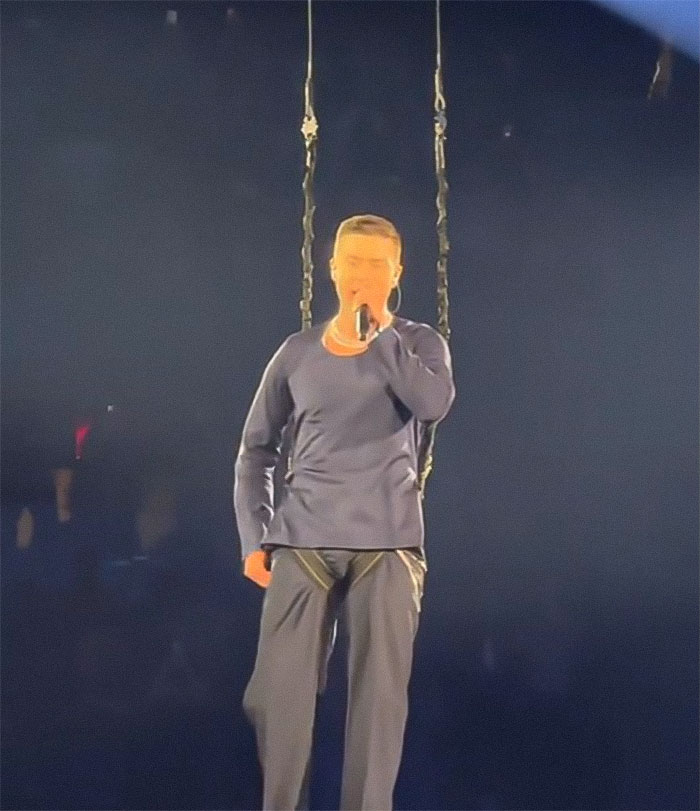 Justin Timberlake on stage in a navy outfit experiencing a wardrobe malfunction, with visible harness attachments. Justin Timberlake on stage in a navy outfit experiencing a wardrobe malfunction, with visible harness attachments.