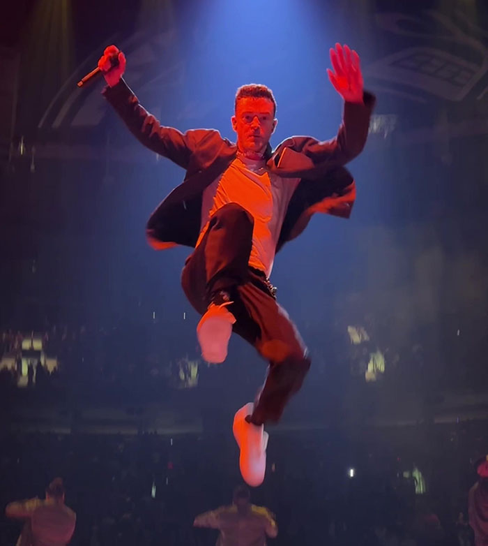 Justin Timberlake mid-air on stage during a live concert, wearing a dynamic outfit. Justin Timberlake mid-air on stage during a live concert, wearing a dynamic outfit.