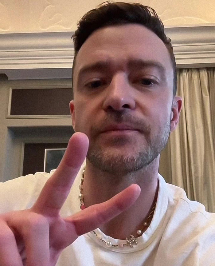 Justin Timberlake poses indoors, wearing a white top, making a peace sign gesture, smiles slightly. Justin Timberlake poses indoors, wearing a white top, making a peace sign gesture, smiles slightly.