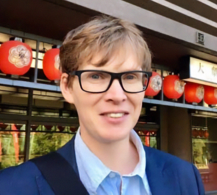 A cultural sociology expert in glasses and a blue shirt stands outside a building. A cultural sociology expert in glasses and a blue shirt stands outside a building.
