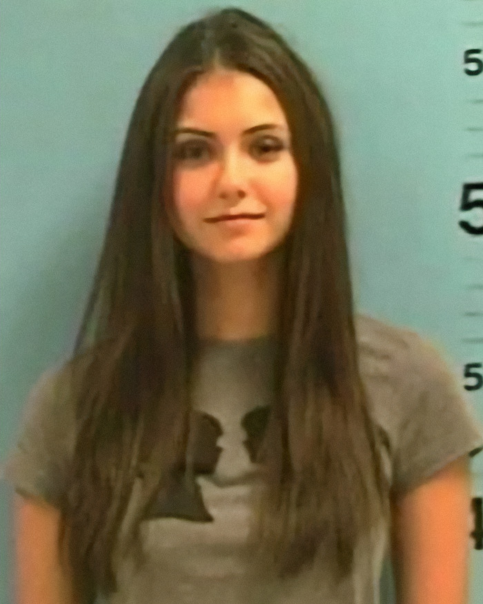 Nina Dobrev in a gray shirt against a height chart background, representing a viral mugshot of a criminal heartthrob. Nina Dobrev in a gray shirt against a height chart background, representing a viral mugshot of a criminal heartthrob.