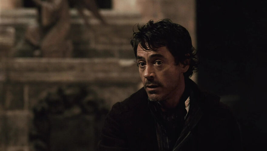 Robert Downey Jr. with dark hair in a somber setting, capturing a contemplative moment, often portraying himself in roles.