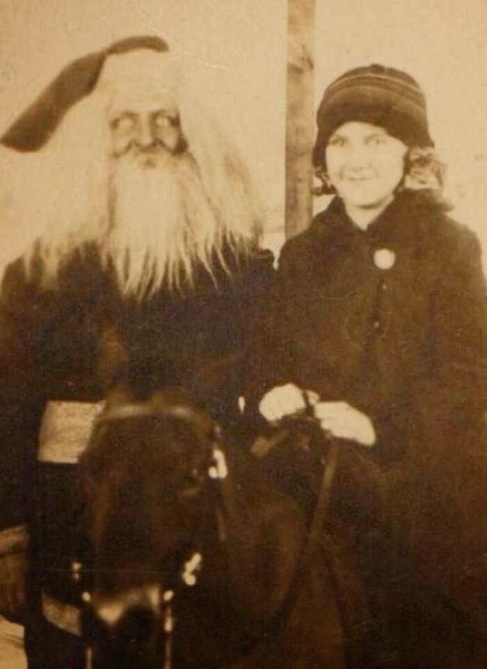 Vintage photo of a creepy Santa with a long beard, standing beside a smiling child on a horse. Vintage photo of a creepy Santa with a long beard, standing beside a smiling child on a horse.