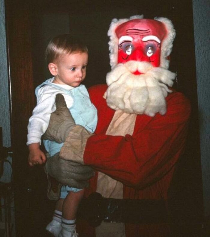 Child held by a creepy Santa with a red face and exaggerated features indoors. Child held by a creepy Santa with a red face and exaggerated features indoors.