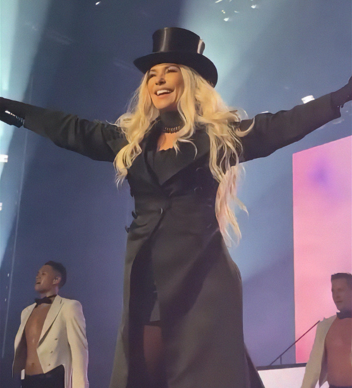 Shania Twain wearing a black top hat, performing energetically under bright lights. Shania Twain wearing a black top hat, performing energetically under bright lights.